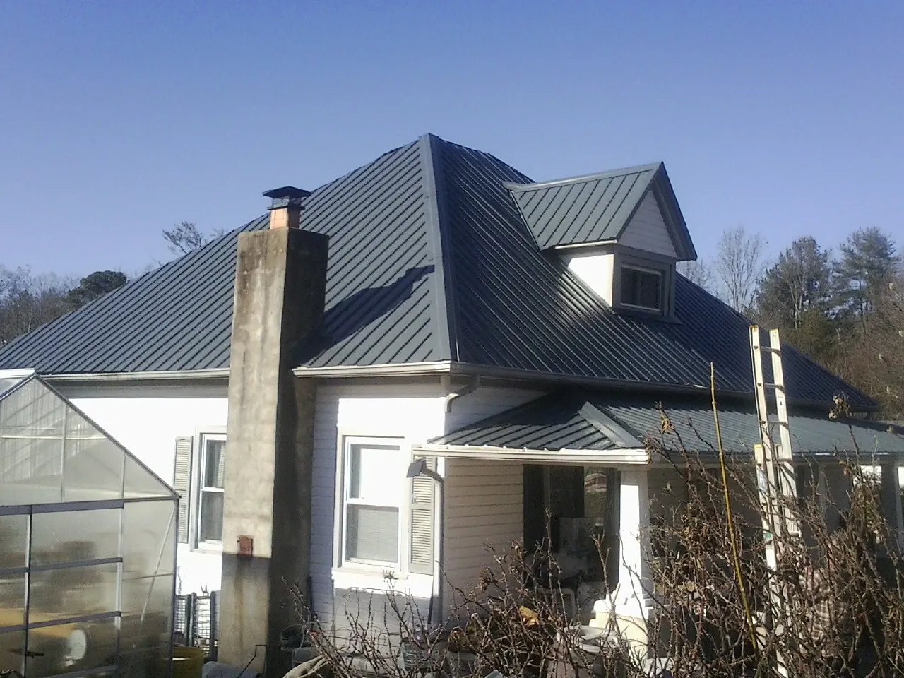 Dark blue standing seam metal roof on a white farmhouse with dormer — Slate & Tile Roof Repair by Roofing Brothers in Bloomfield