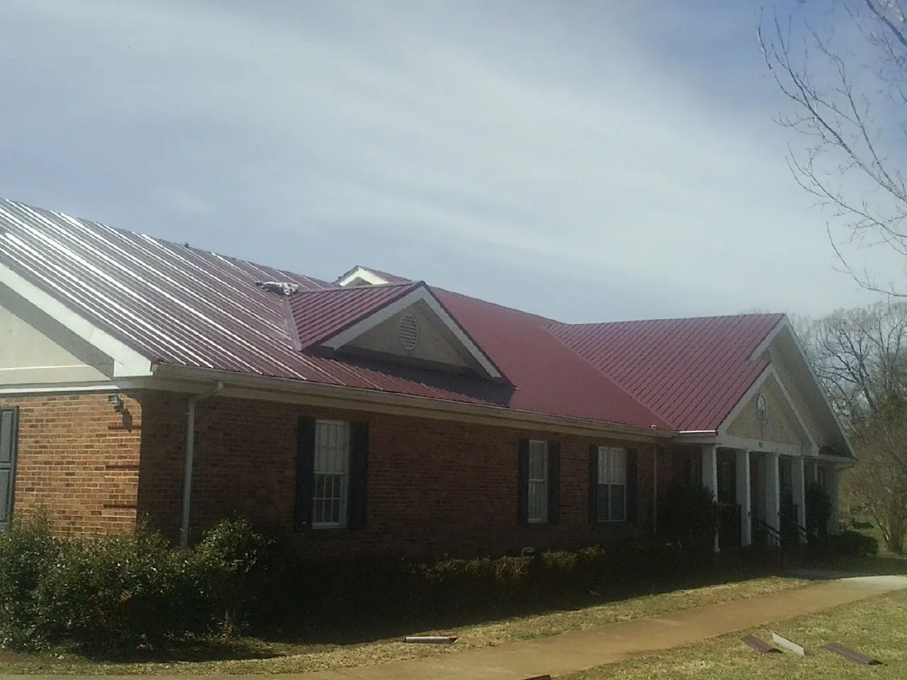 Red metal roof with gabled entries on a long brick building, from a Hail Damage Roof Repair job in Bloomfield