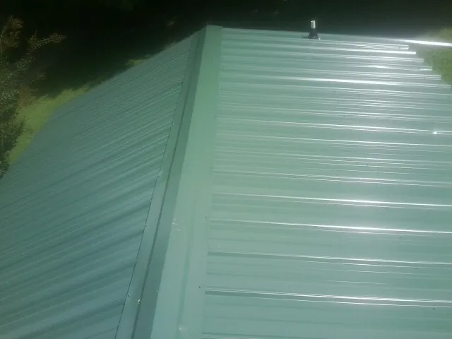 New green metal panels meeting at the ridge of a roof — Flat Roof Repair work by our crew in Bloomfield
