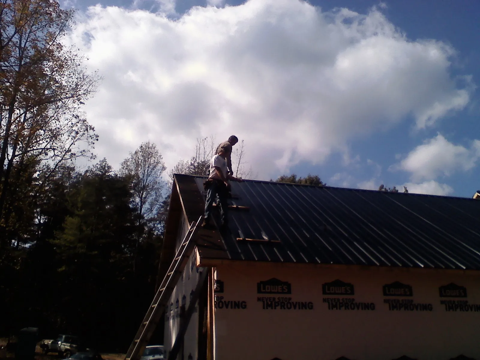 Roofer fastening dark metal panels high against a cloudy sky, from a Roof Inspection job in Bloomfield